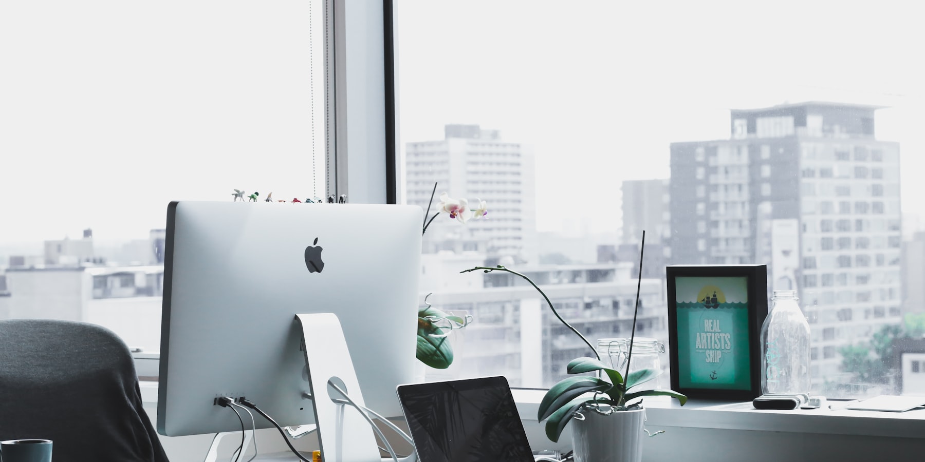 A dedicated desk by the window, with a monitor, plant and the city beyond